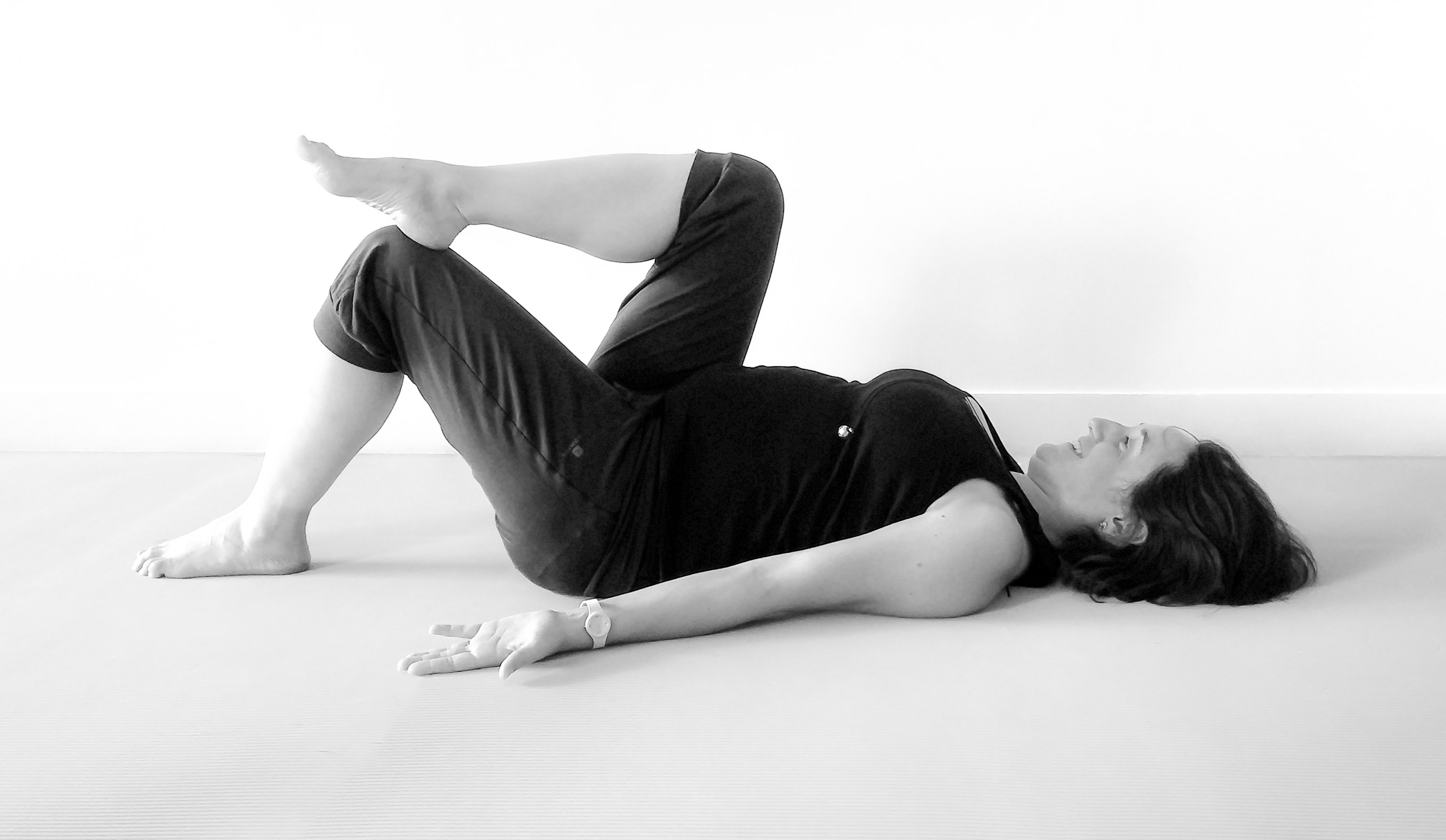 Future maman sur le dos, une jambe en appui lors d'un cours de Yoga prénatal